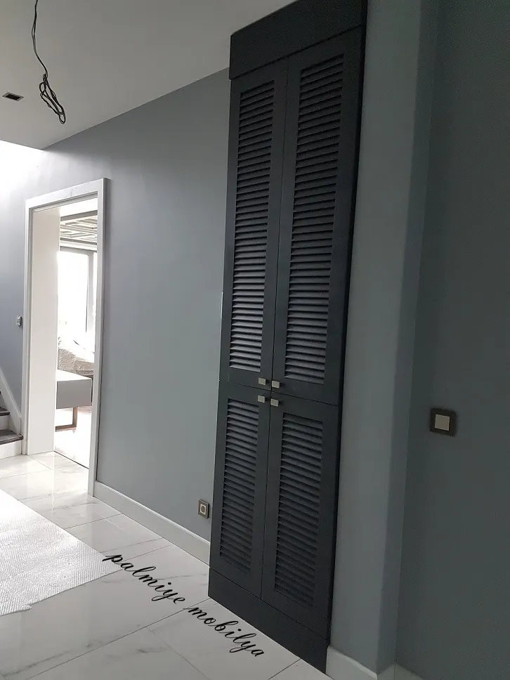 Koridorda tavana kadar uzanan antrasit panjur kapaklı lake dolap ve beyaz kapı pervazı